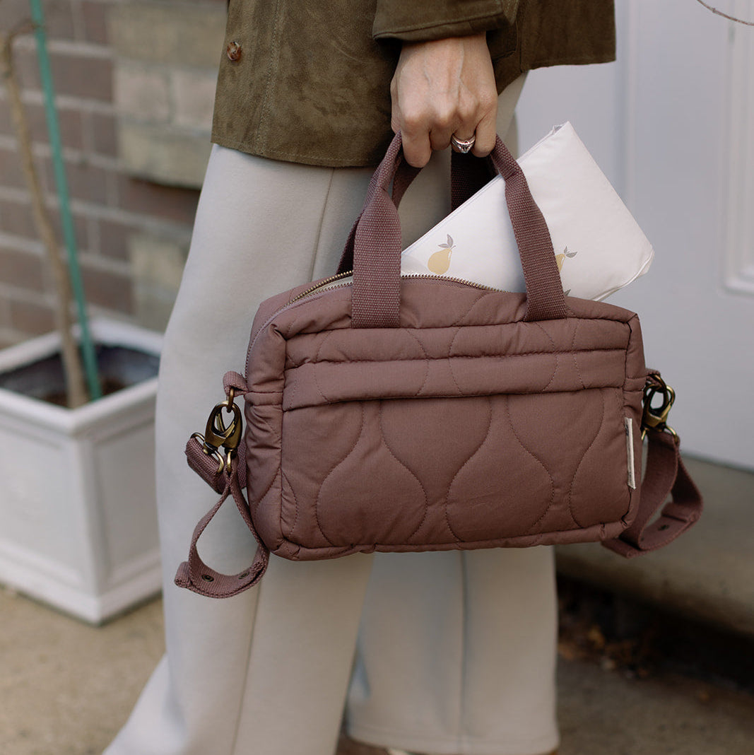Person holding a brown quilted handbag with a neutral background