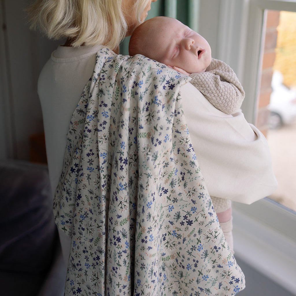 Woman holding a baby wrapped in a floral blanket by a window