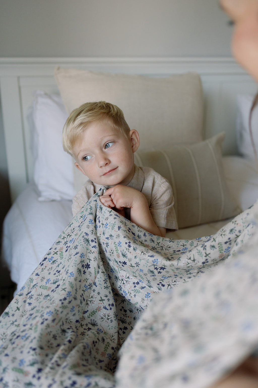 Child lying on a bed with a floral blanket, looking up at an adult.