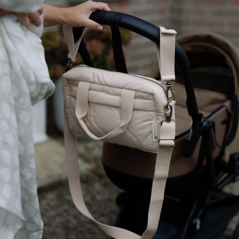 Person holding a beige quilted handbag next to a baby stroller outdoors.