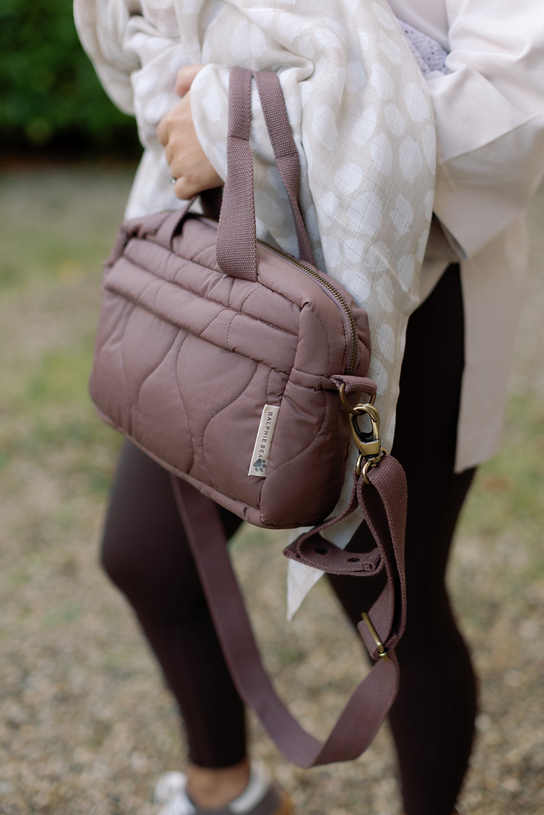 Person holding a quilted brown handbag with a blurred background
