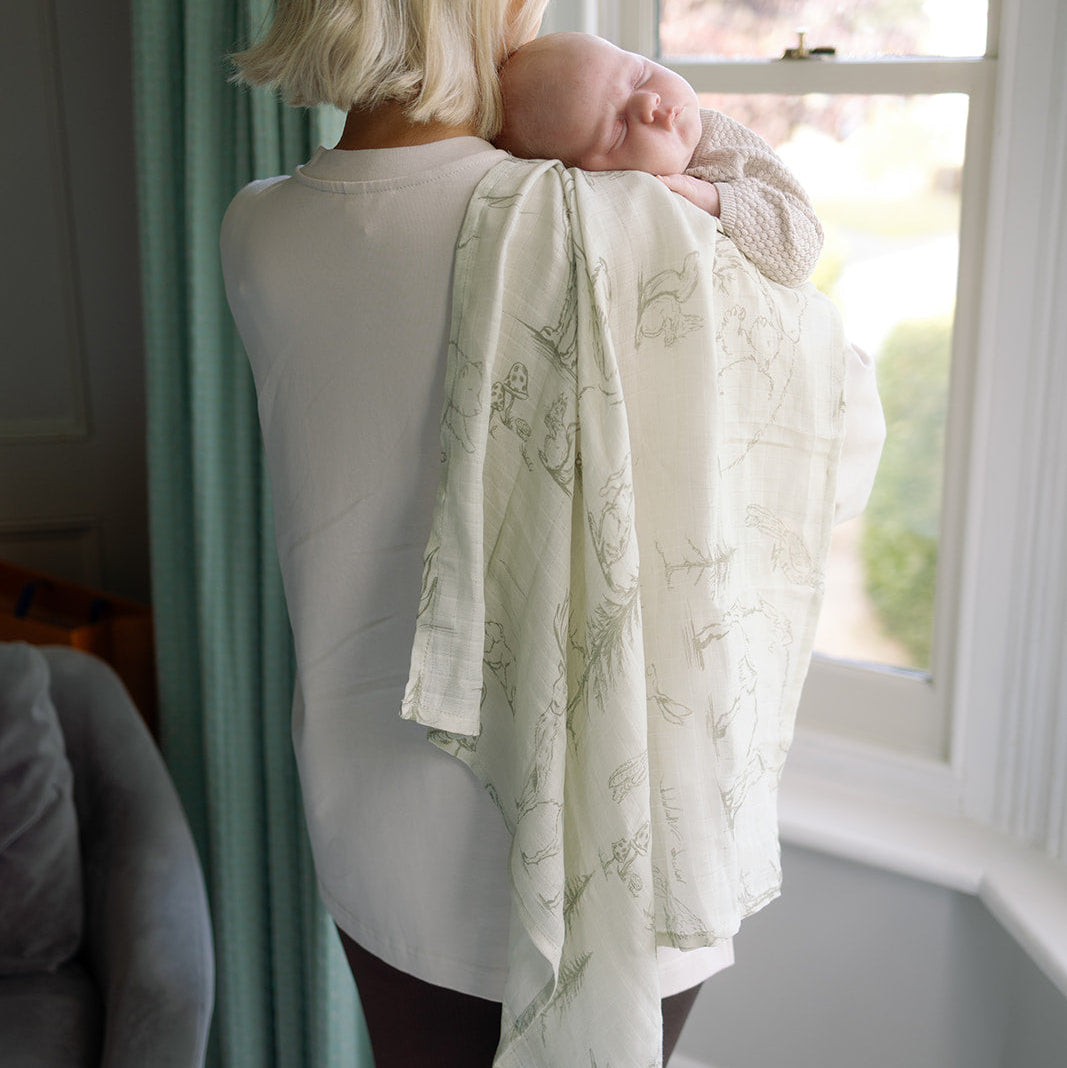 Woman holding a baby wrapped in a patterned blanket by a window