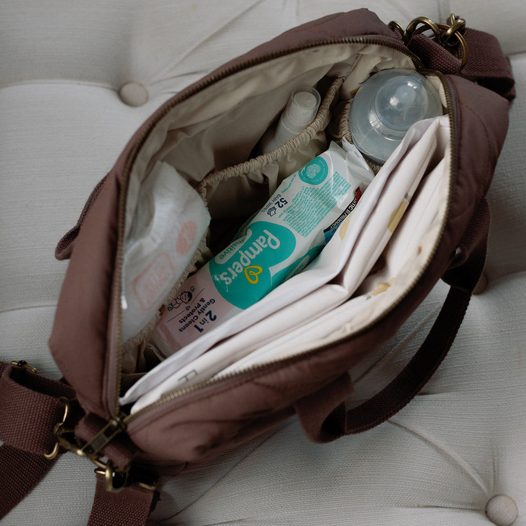 Open brown diaper bag with baby items on a white cushioned surface