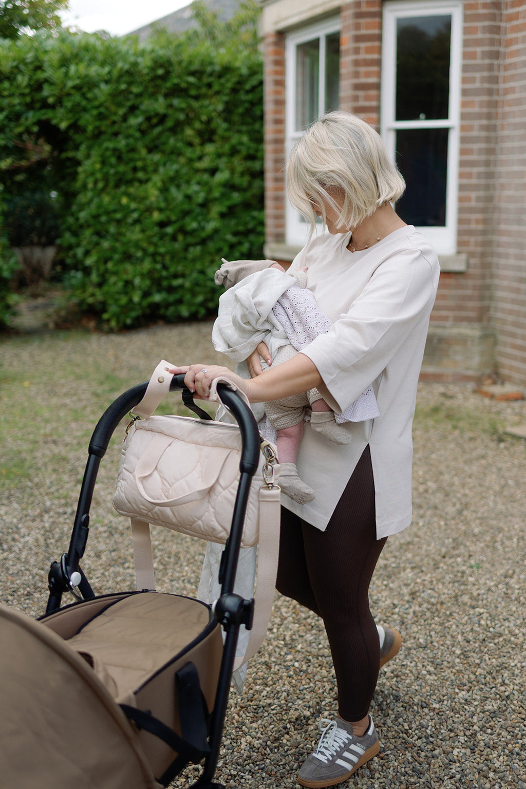 Woman pushing a stroller and holding a baby outdoors.