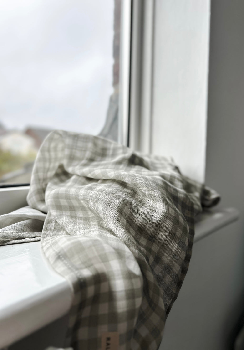 Plaid towel draped over a window sill with a blurred outdoor background
