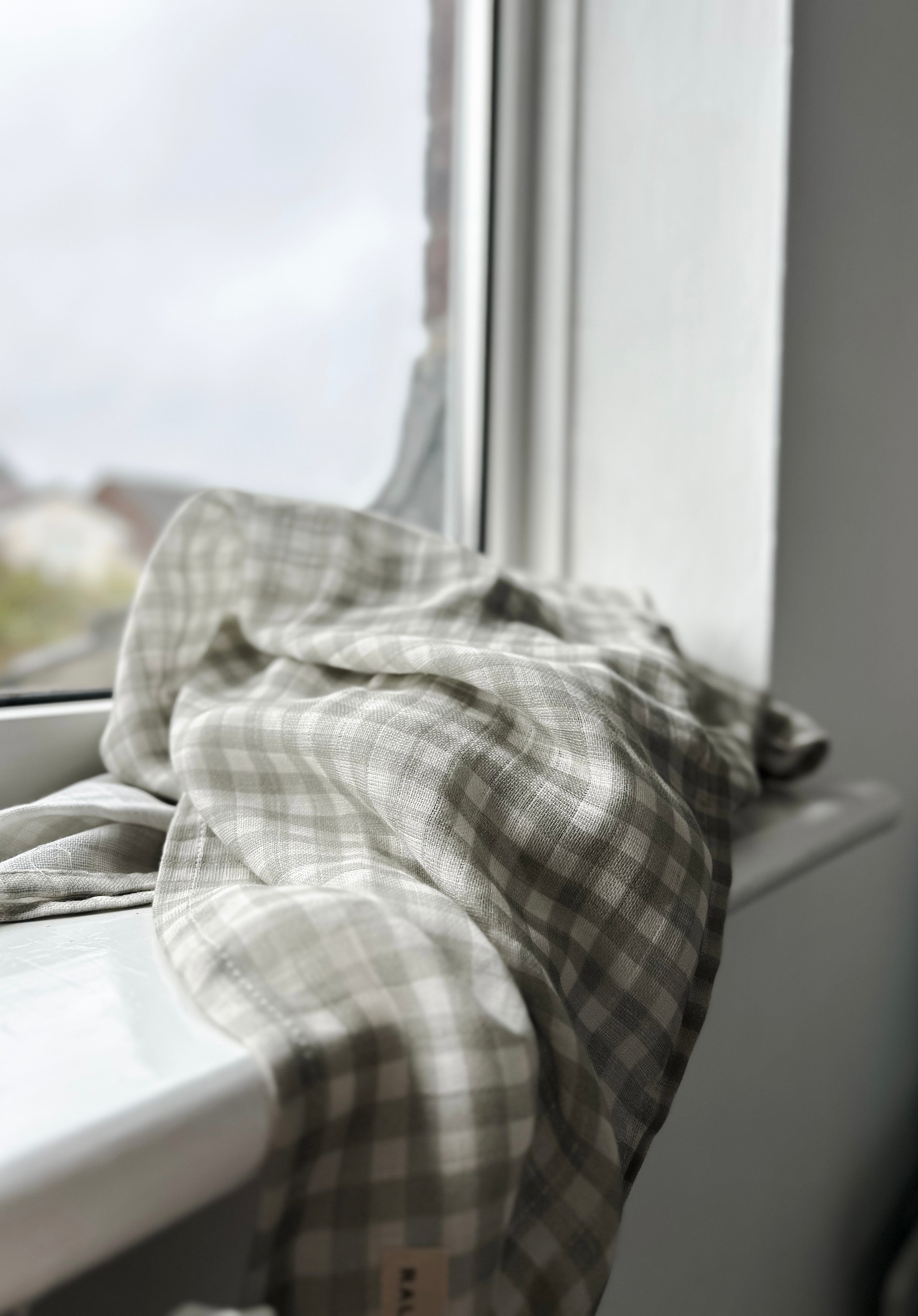 Plaid towel draped over a window sill with a blurred outdoor background