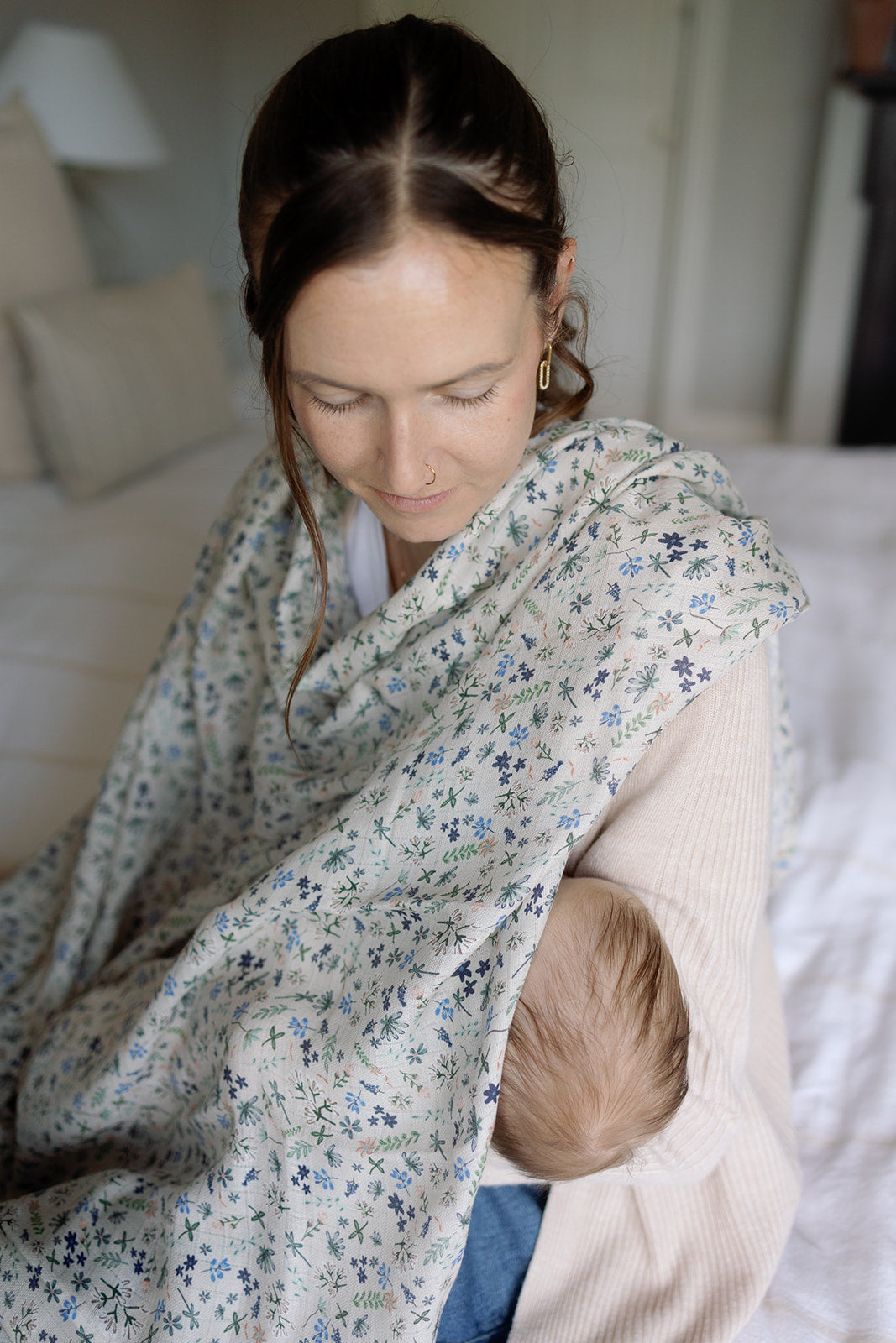Woman holding a baby wrapped in a floral blanket in a bedroom setting