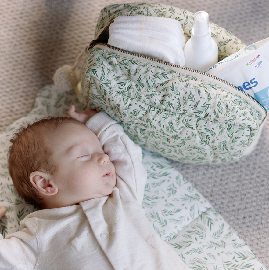 Baby lying next to a green patterned diaper bag with baby items inside