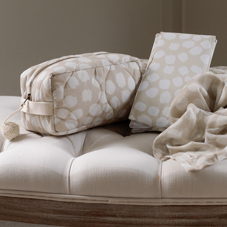 Beige polka dot bag and pillow on a beige sofa with a neutral background