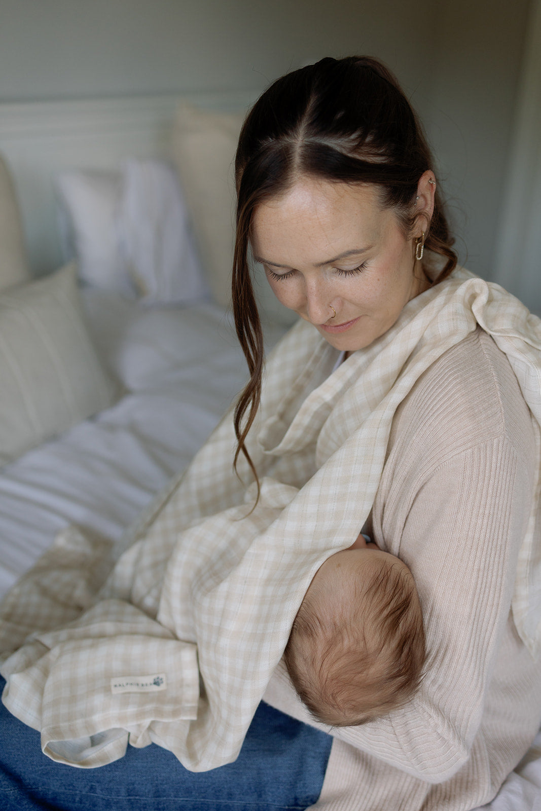 Woman breastfeeding a baby wrapped in a beige blanket with a visible brand logo.