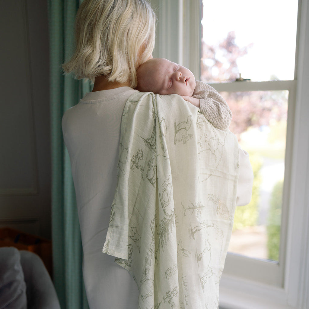 Woman holding a baby wrapped in a patterned blanket by a window
