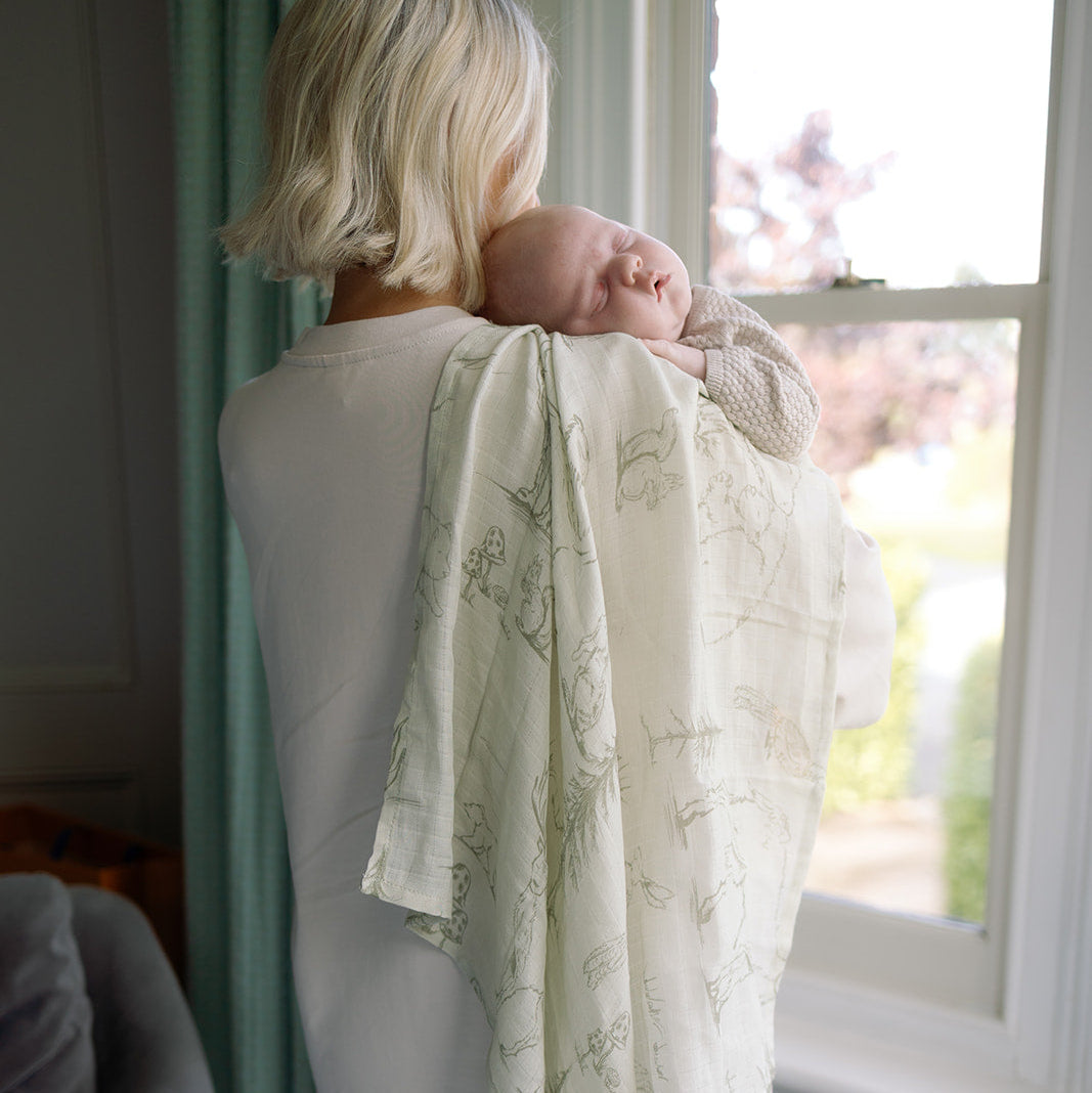 Woman holding a baby wrapped in a patterned blanket by a window