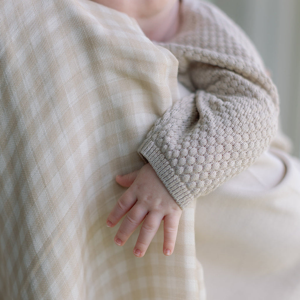 Close-up of a child's hand holding a textured fabric, with a blurred background.