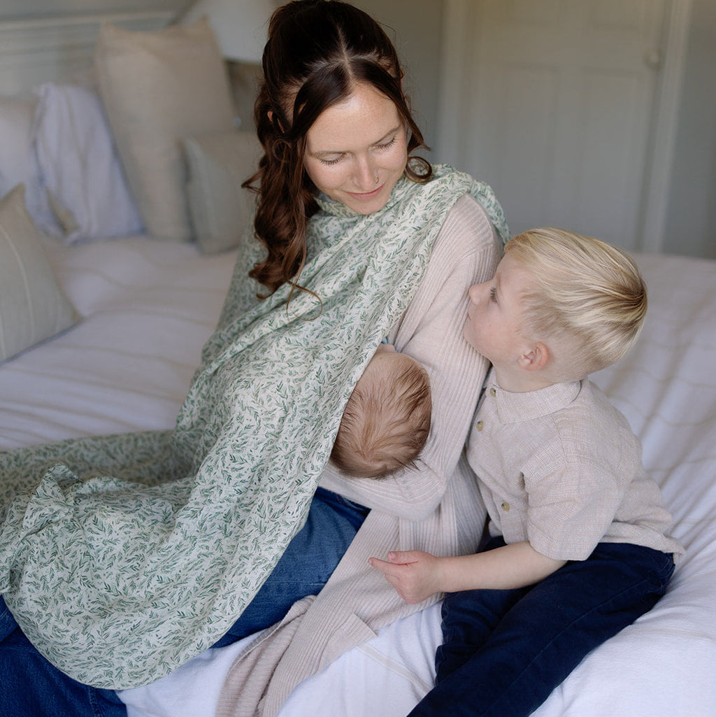 Woman sitting on a bed with two children, one of whom is being held by the woman.