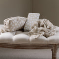 Beige cushion with a patterned bag and blanket on a wooden bench against a plain wall.