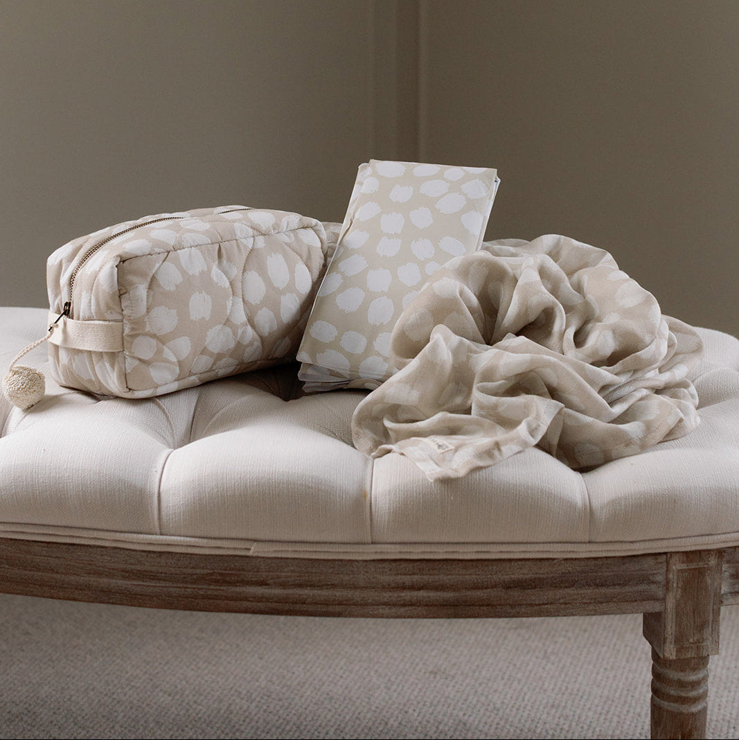 Beige cushion with a patterned bag and blanket on a wooden bench against a plain wall.