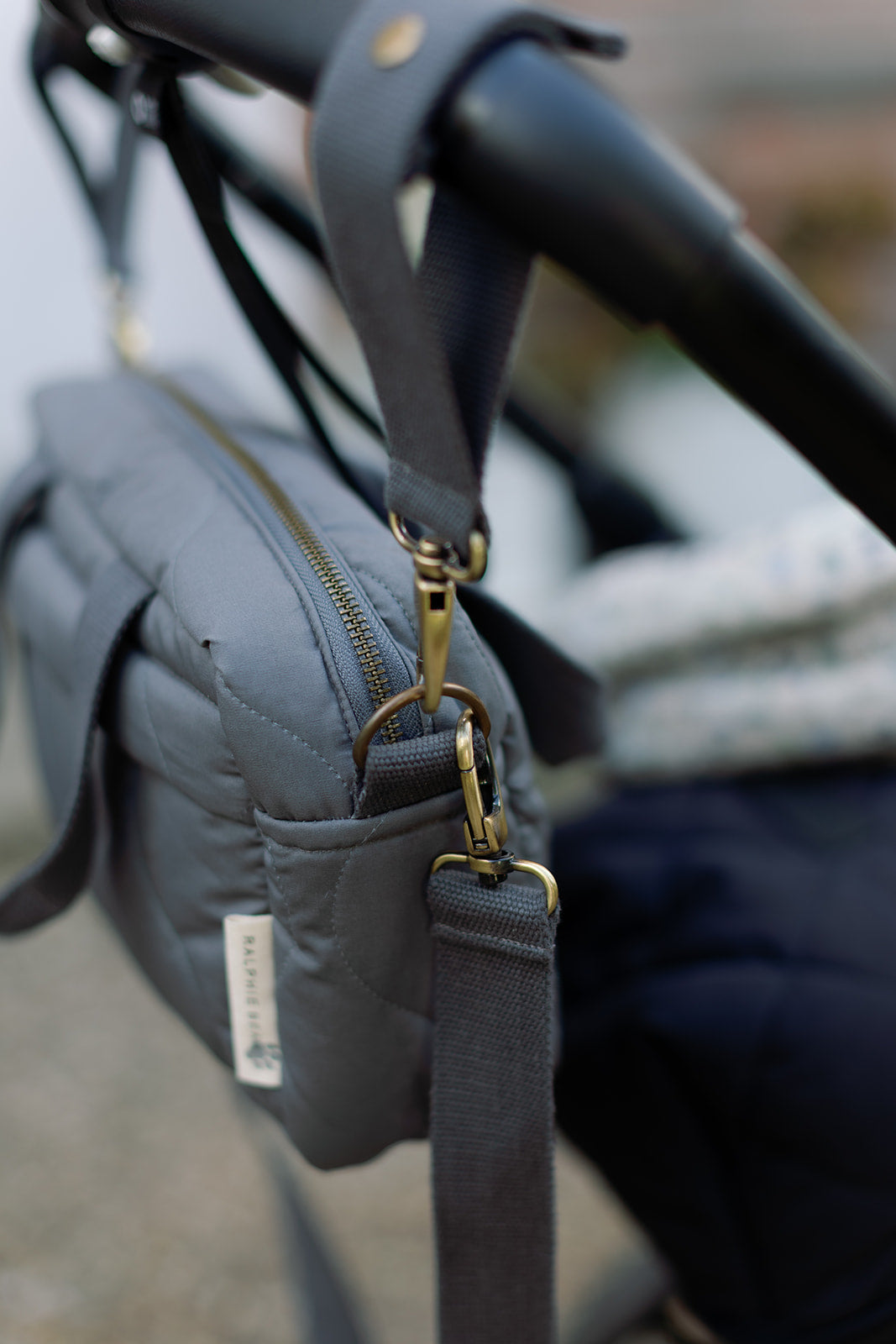 Gray quilted bag with gold hardware attached to a black stroller handle.