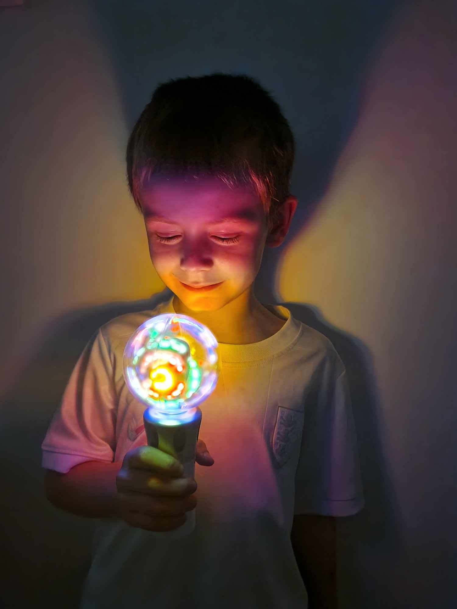 Child holding a colorful light bulb in a dark setting