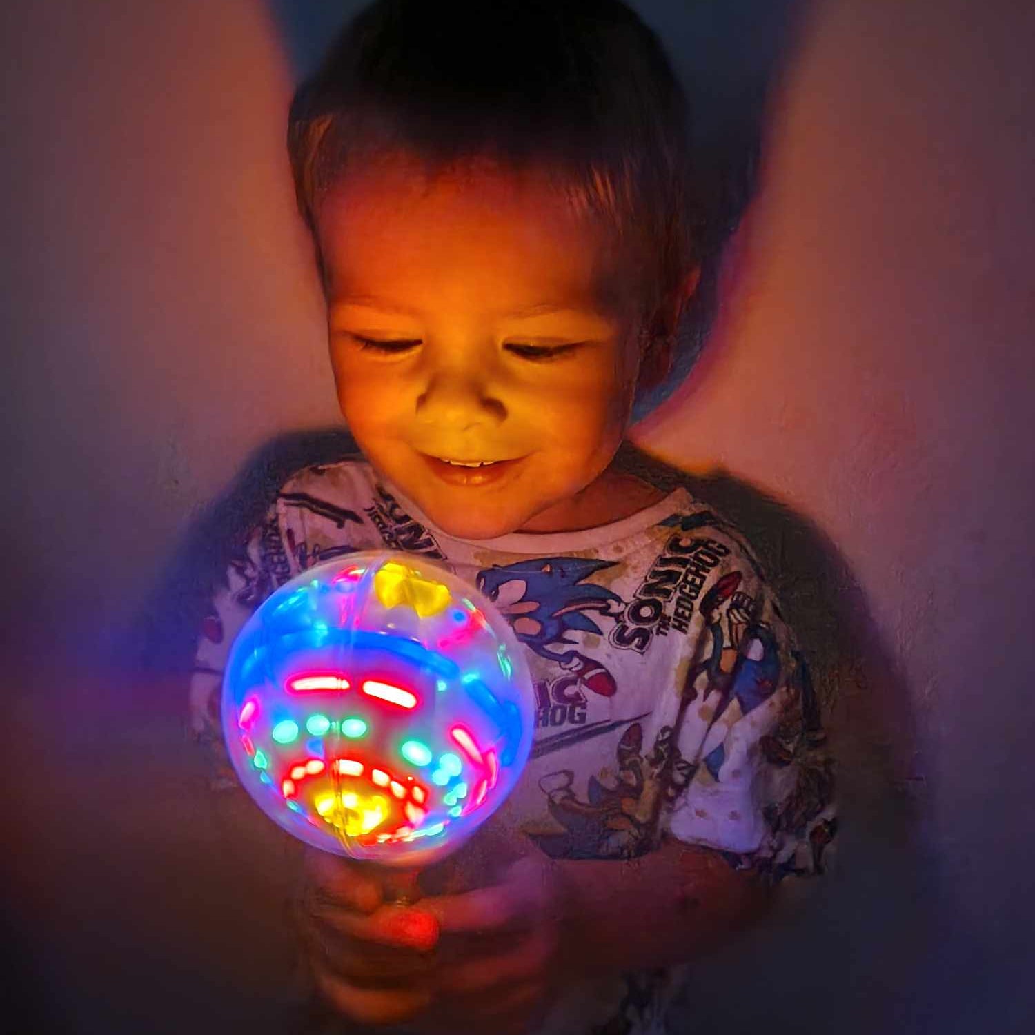 Child holding a colorful发光球 in a dimly lit room