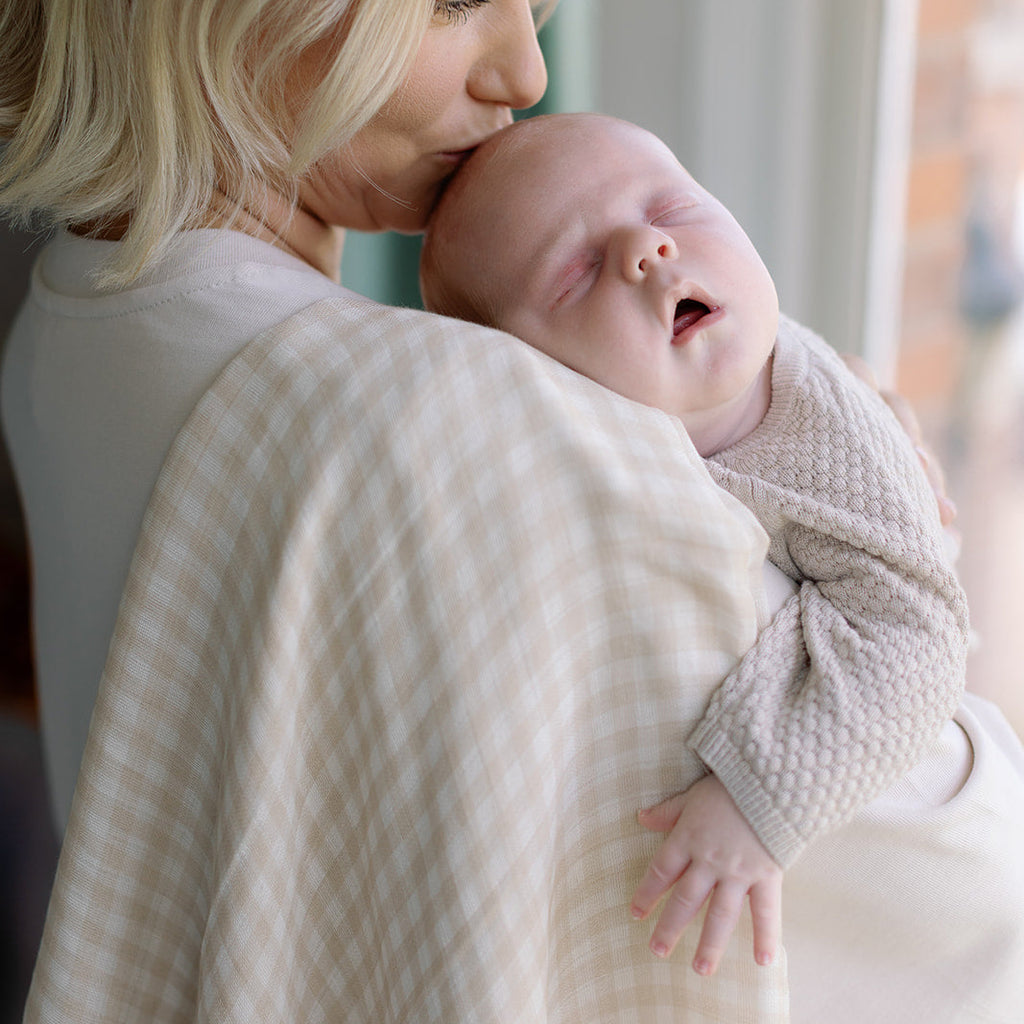 Woman holding a baby wrapped in a textured blanket indoors.