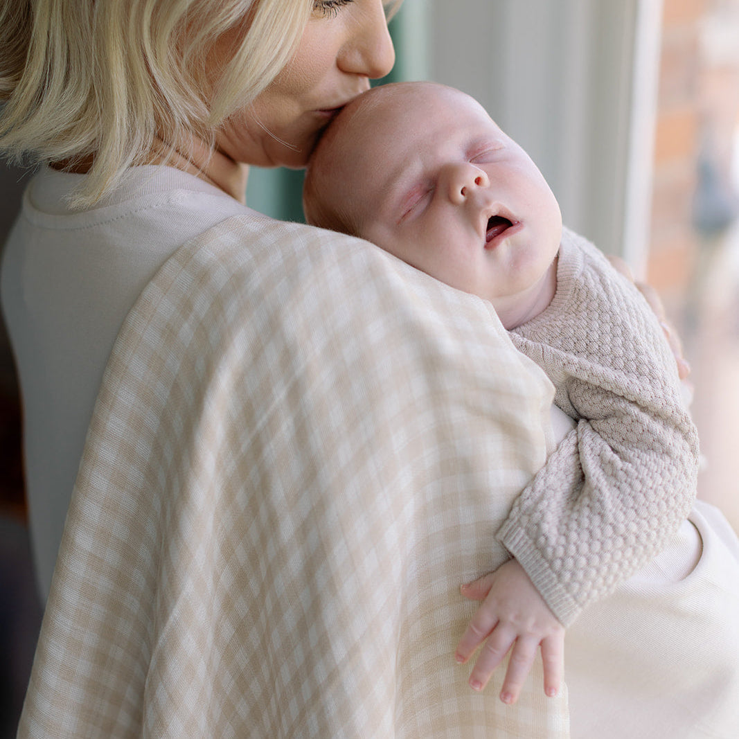 Woman holding a baby wrapped in a textured blanket indoors.