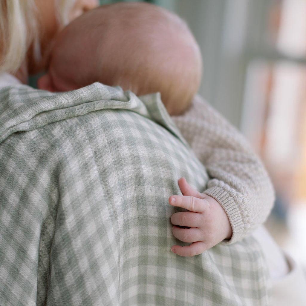 Person holding a baby close, wearing a green checkered garment.