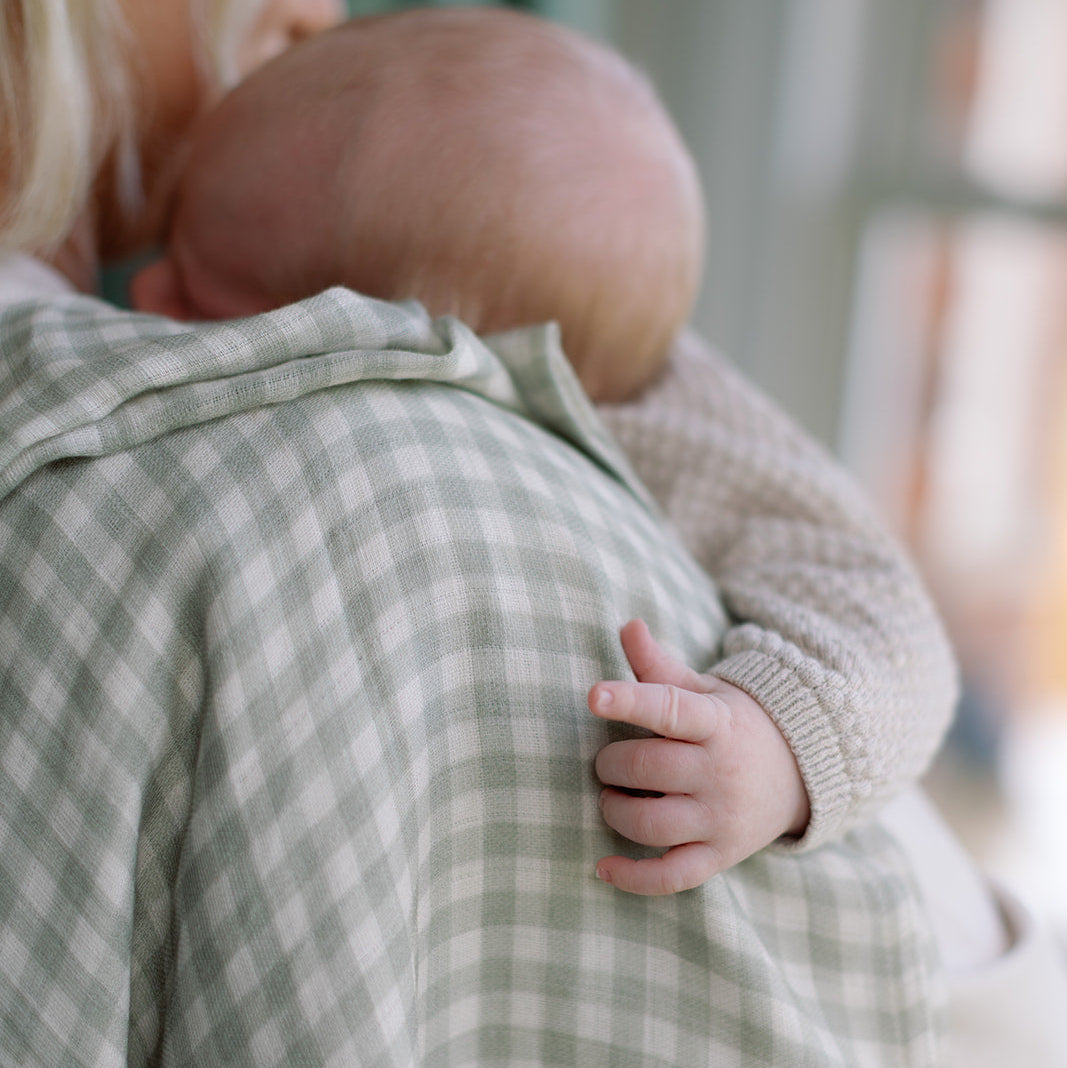 Person holding a baby close, wearing a green checkered garment.