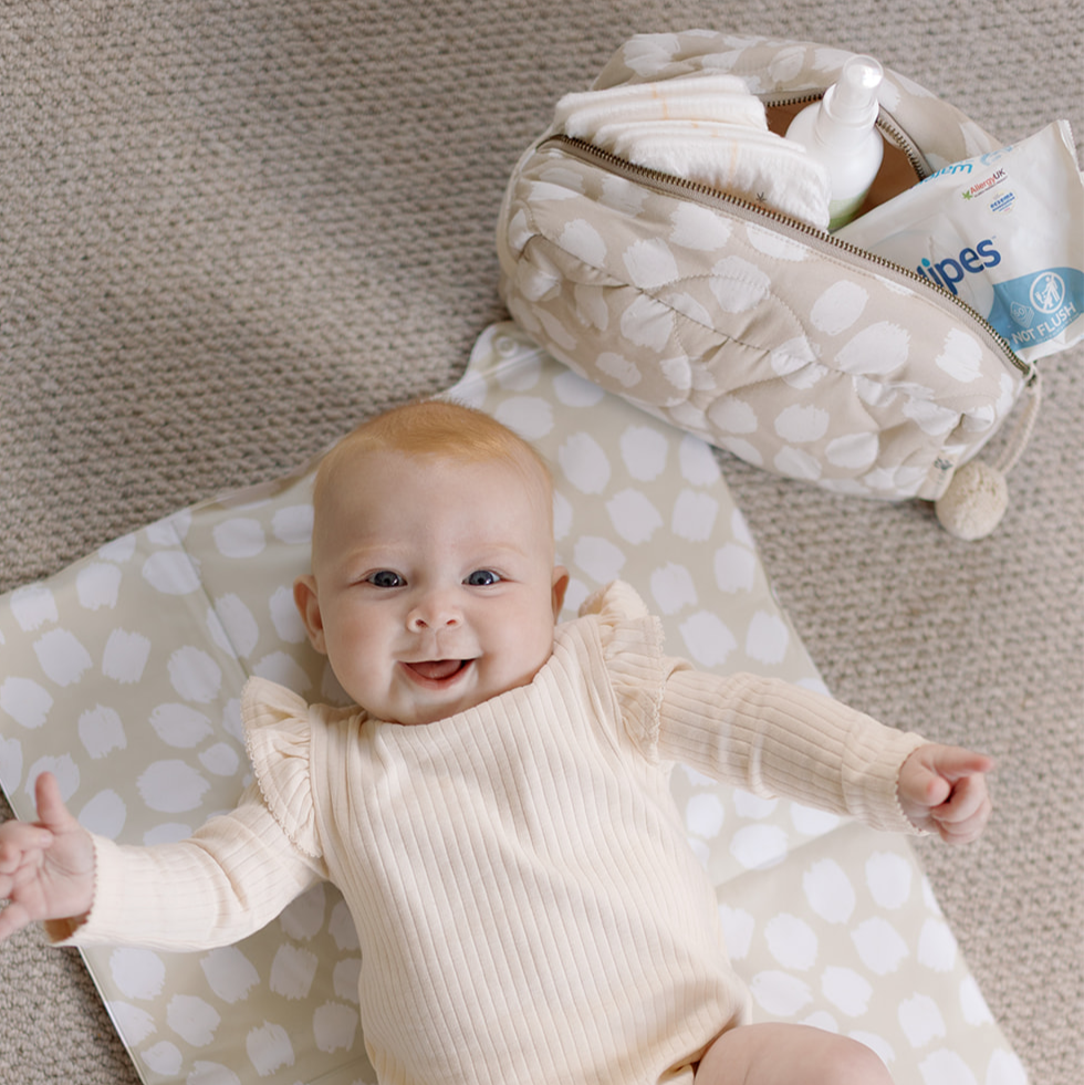 Baby lying on a polka dot blanket with a diaper bag and baby wipes in the background.