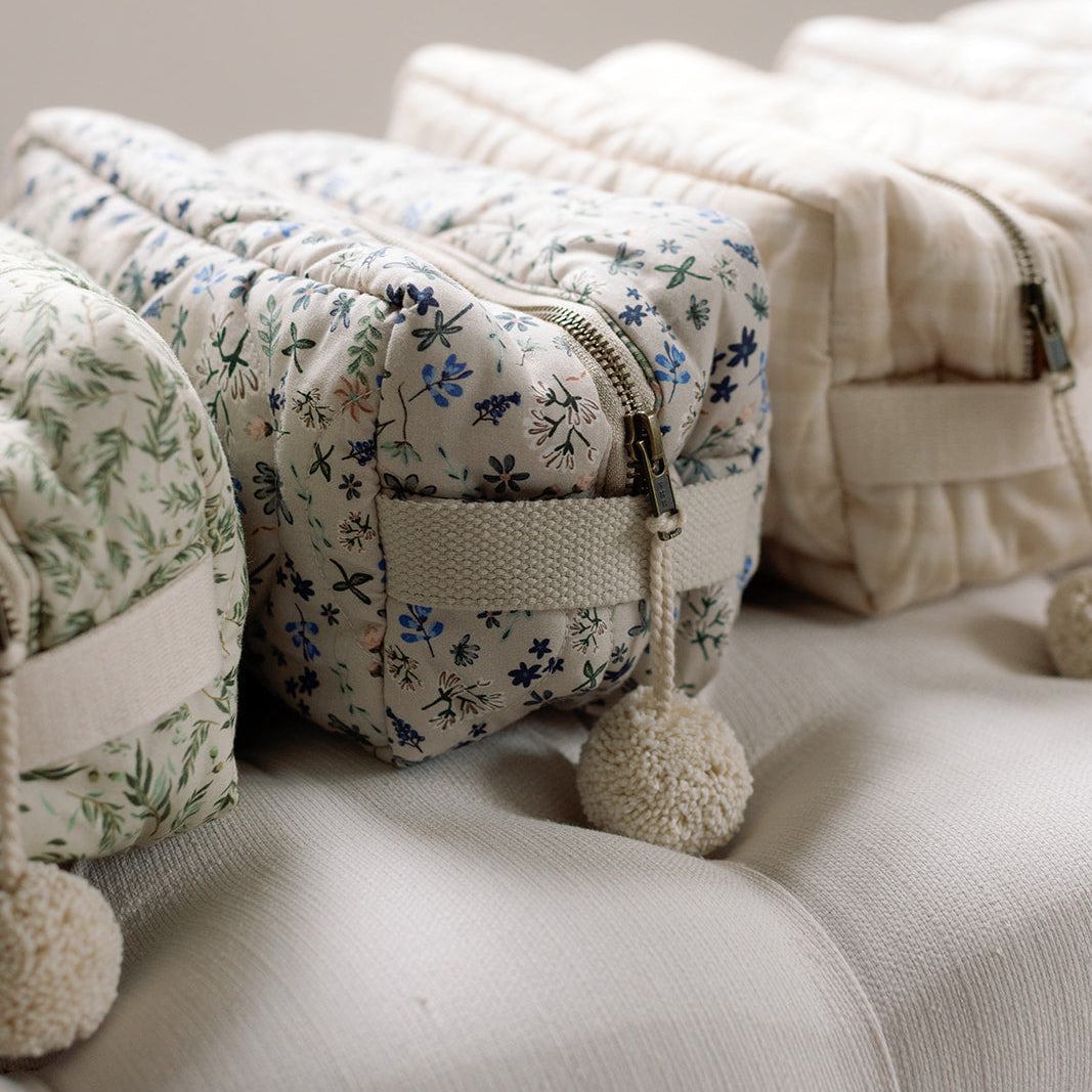 Floral-patterned pouch with pom-pom on a beige sofa