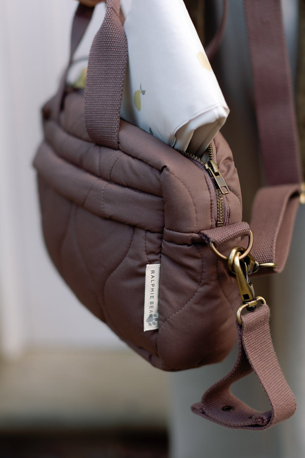 Brown quilted bag with gold zipper and strap on a blurred background