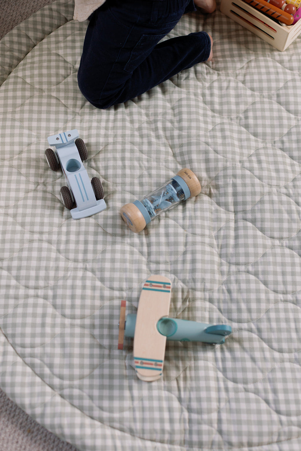 Wooden toys on a checkered blanket with a child partially visible.