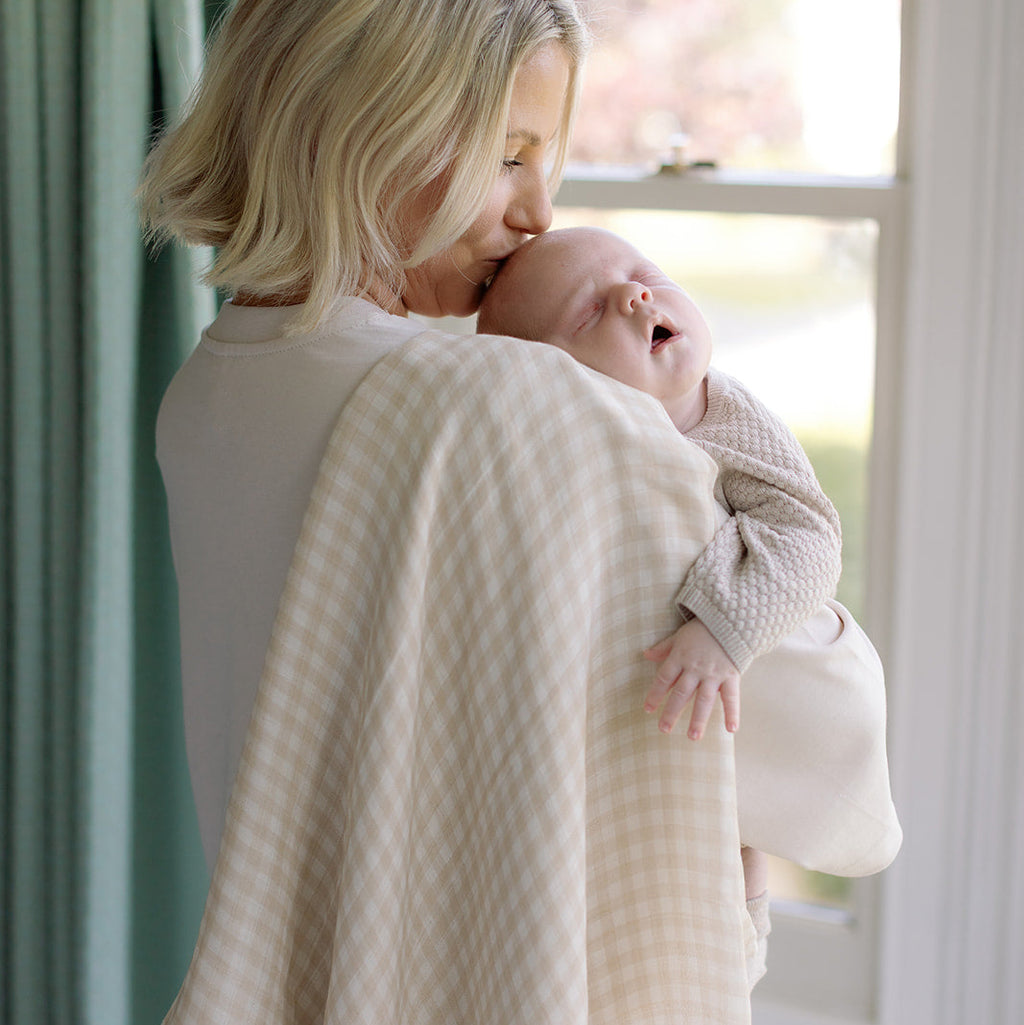 Woman holding a baby wrapped in a textured blanket by a window