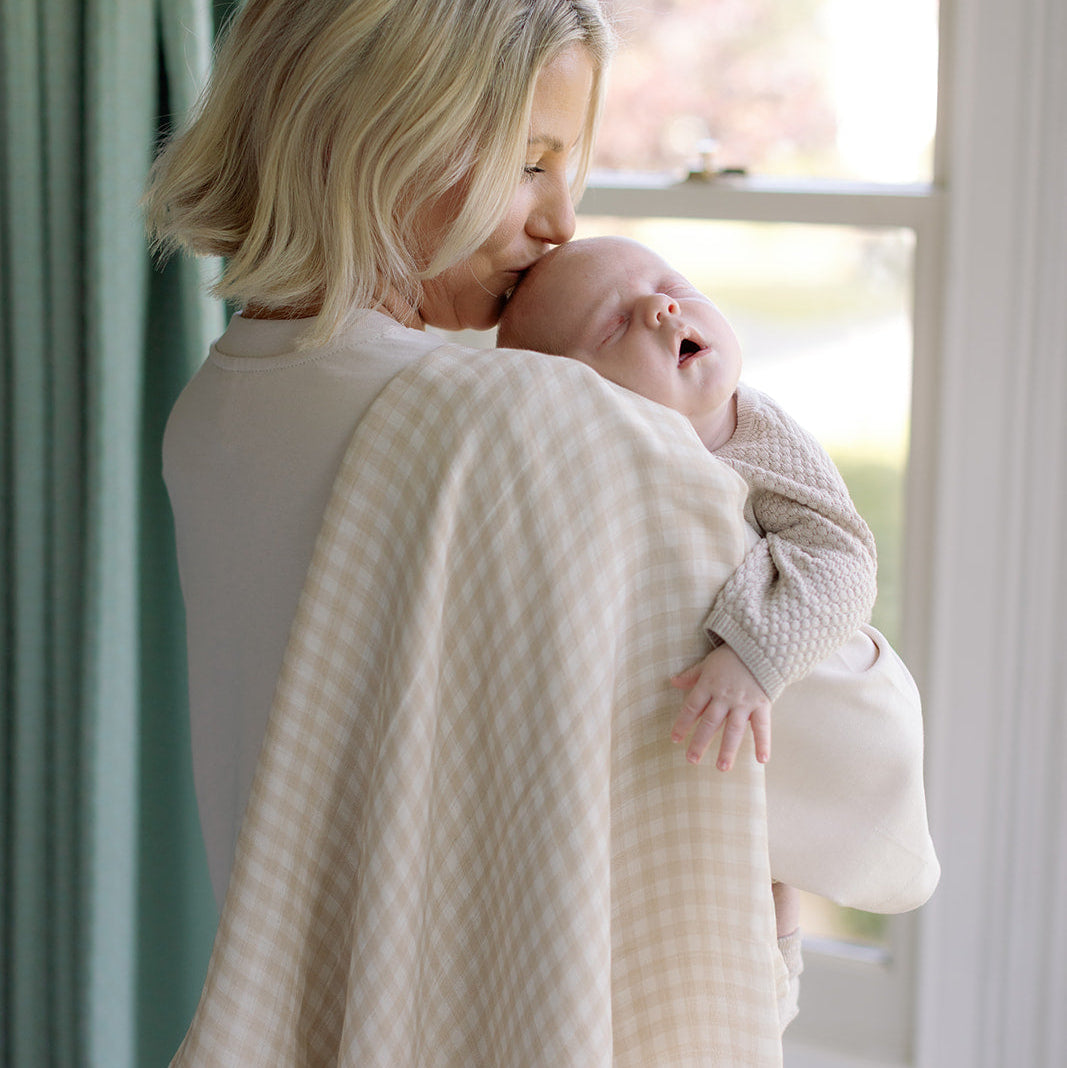 Woman holding a baby wrapped in a textured blanket by a window
