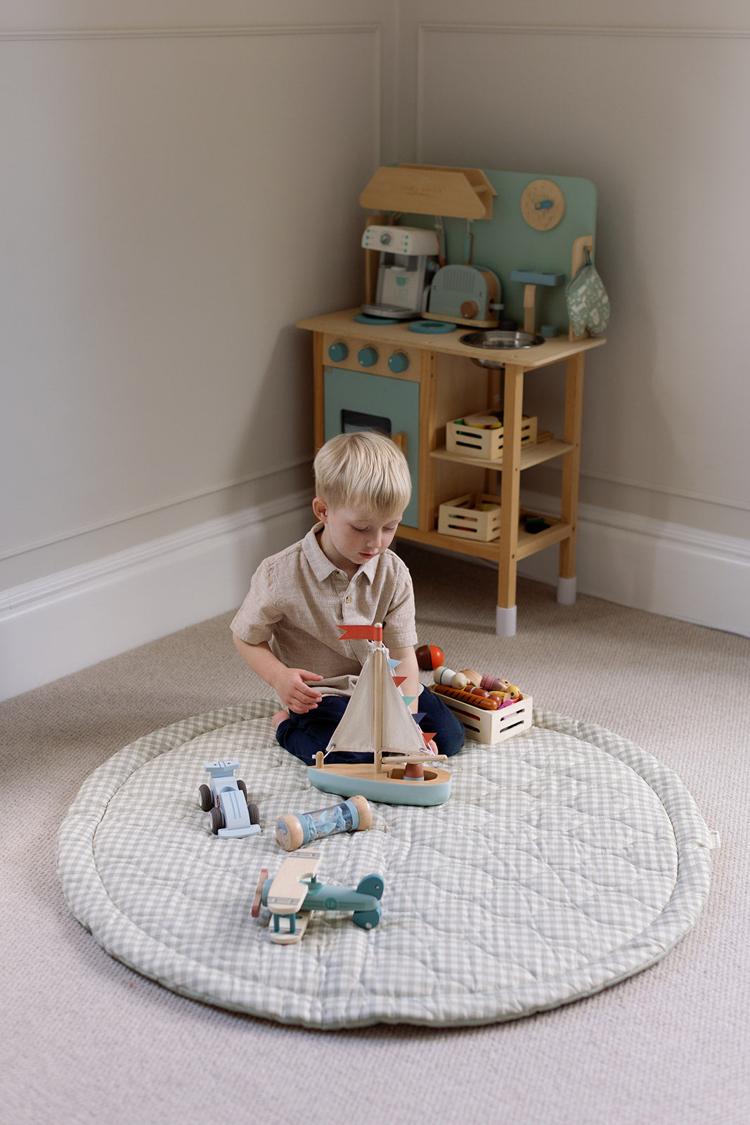 Child playing with toys on a patterned rug in a room with a wooden play kitchen.