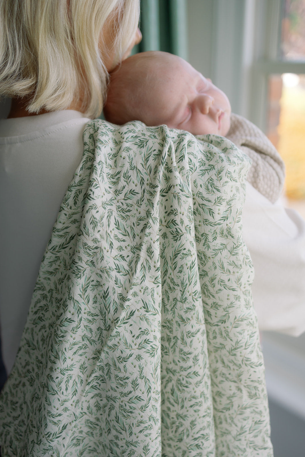 Person holding a baby wrapped in a green patterned blanket indoors.