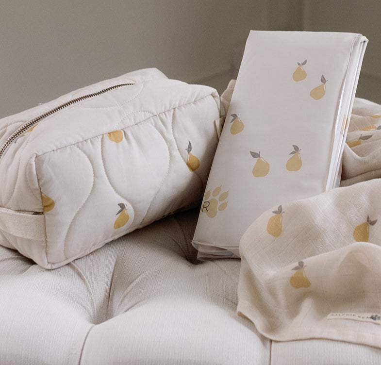 Baby blanket, pillow, and book with pear pattern on a neutral background