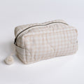 Beige quilted pouch with a small pom-pom on a light gray background