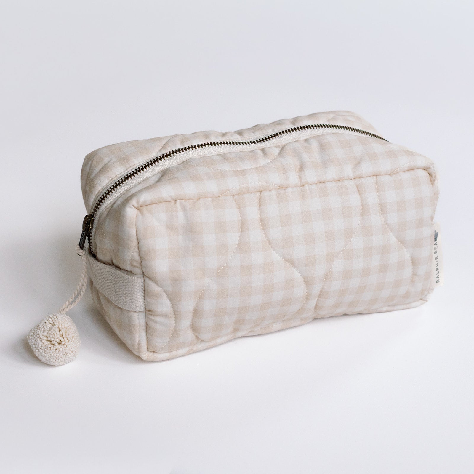 Beige quilted pouch with a small pom-pom on a light gray background