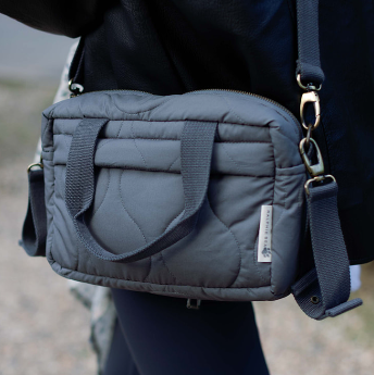Gray quilted bag with a strap held by a person against a blurred background