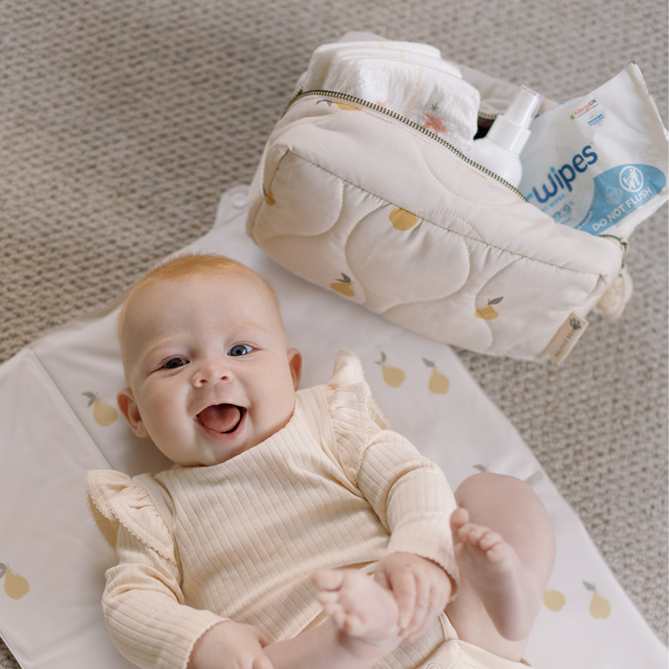 Baby lying on a changing mat with a diaper bag and wipes in the background