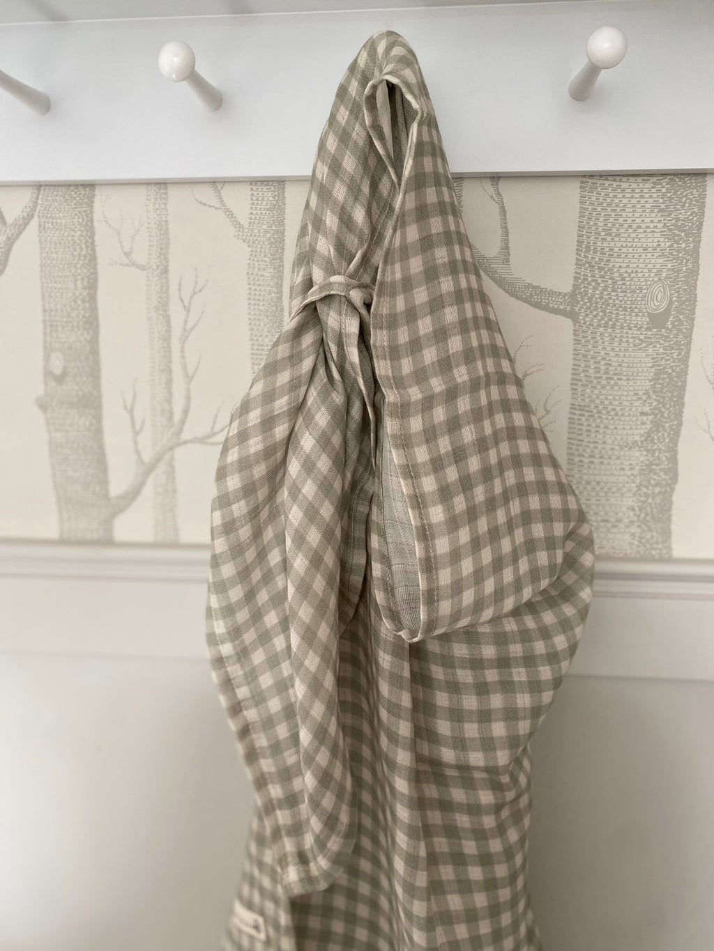 Plaid fabric hanging on a hook against a wall with a nature-themed wallpaper.