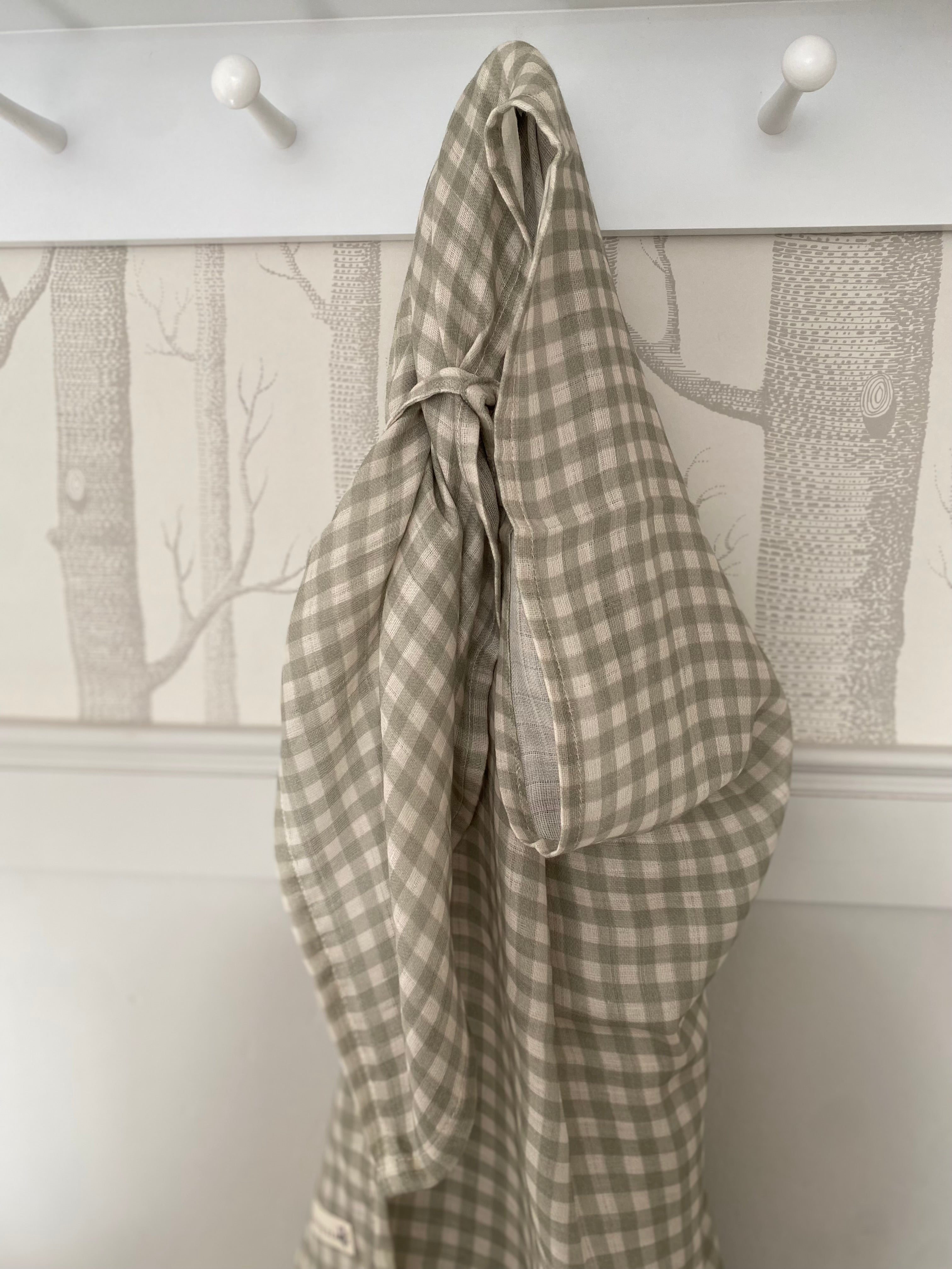 Plaid fabric hanging on a hook against a wall with a nature-themed wallpaper.