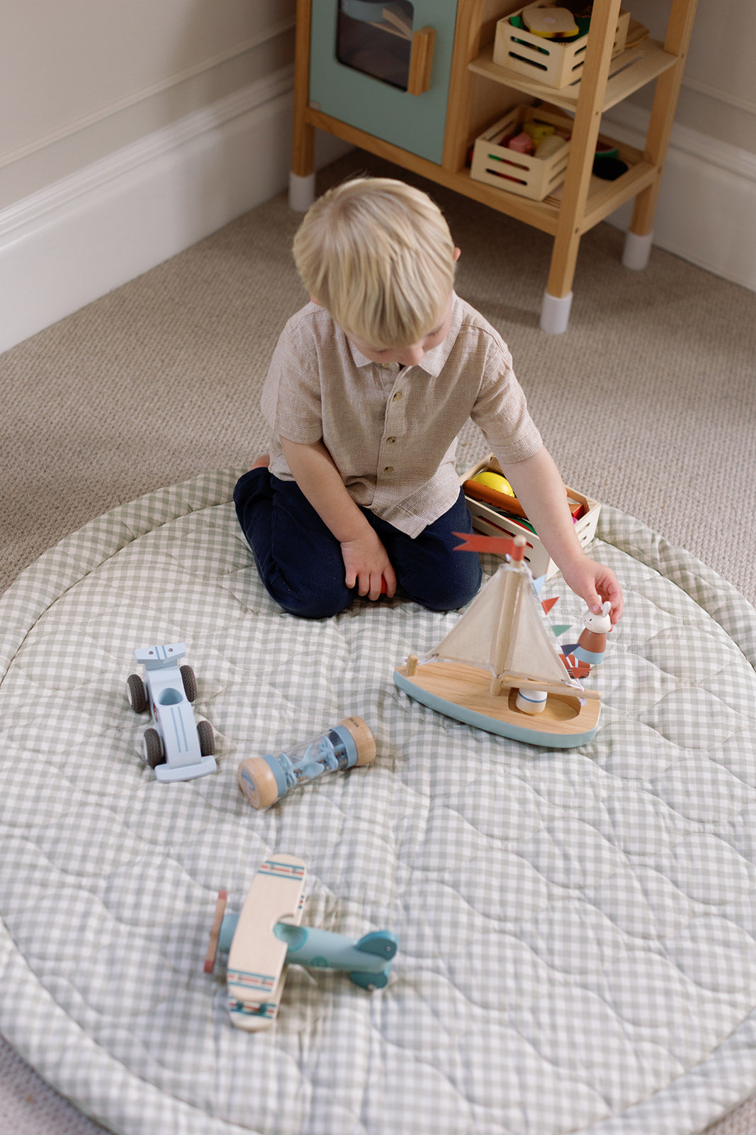 Child playing with wooden toys on a checkered play mat in a room with a wooden shelf.