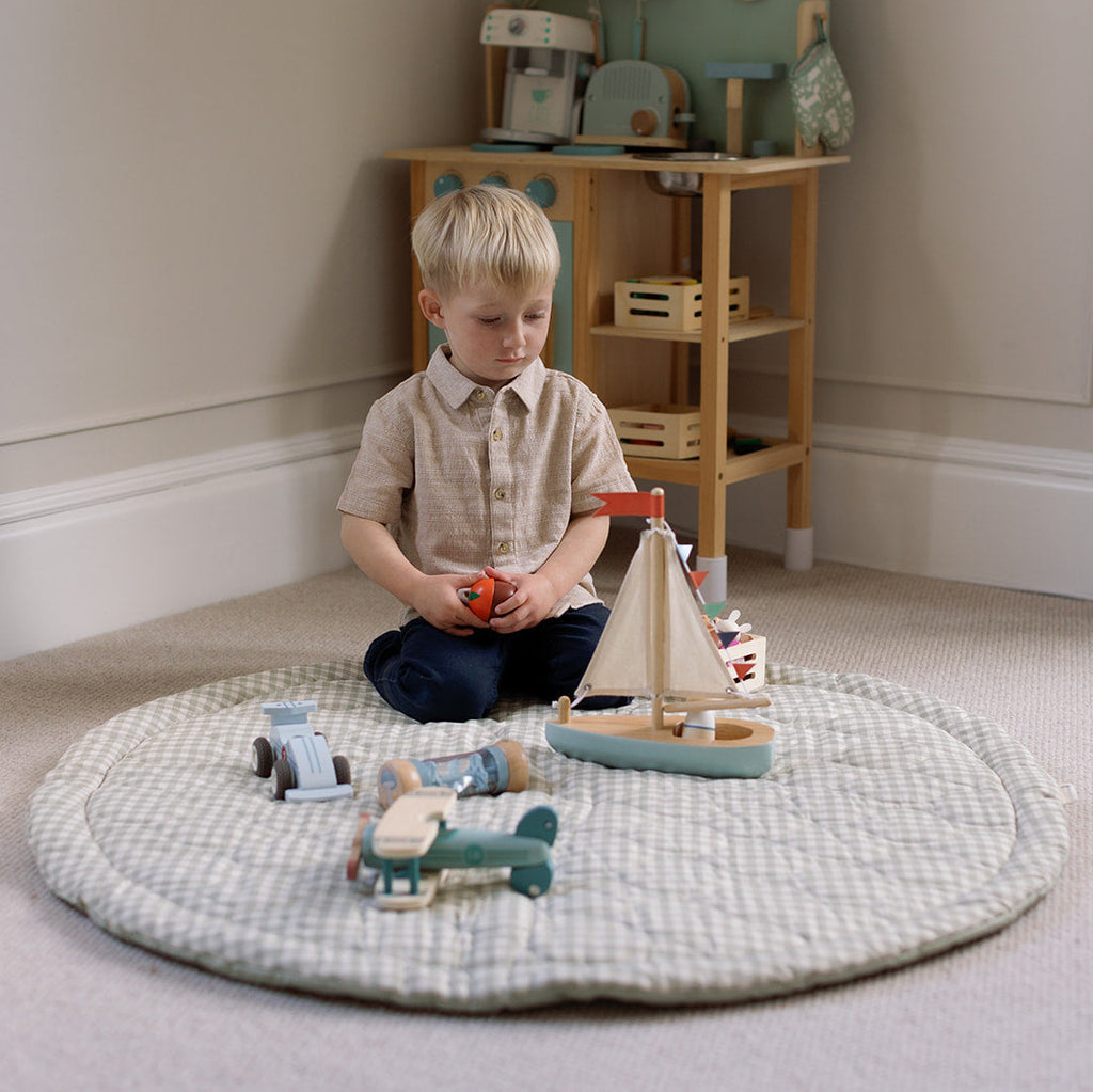 Child playing with toys on a round mat in a room with wooden furniture.