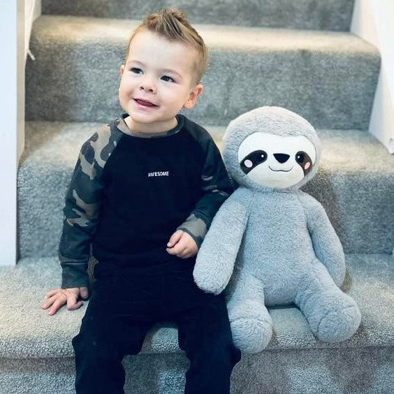 Child sitting on stairs holding a large plush sloth toy