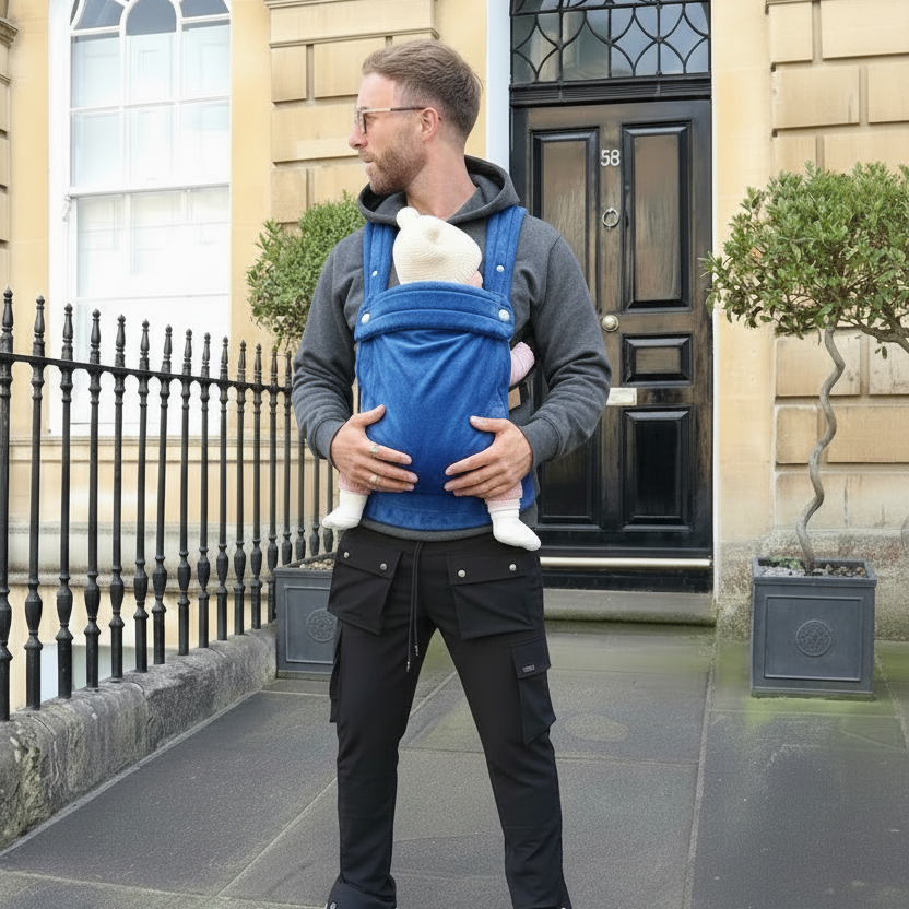 Man carrying a baby in a blue sling outside a building