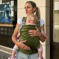 Woman carrying a baby in a green sling outdoors.