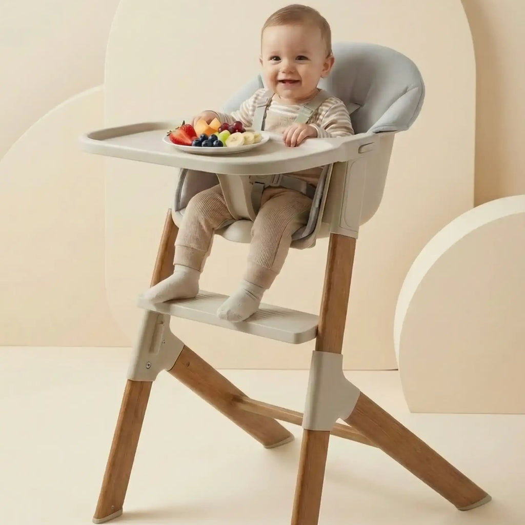 Baby sitting in a modern high chair with a tray of fruits on a neutral background