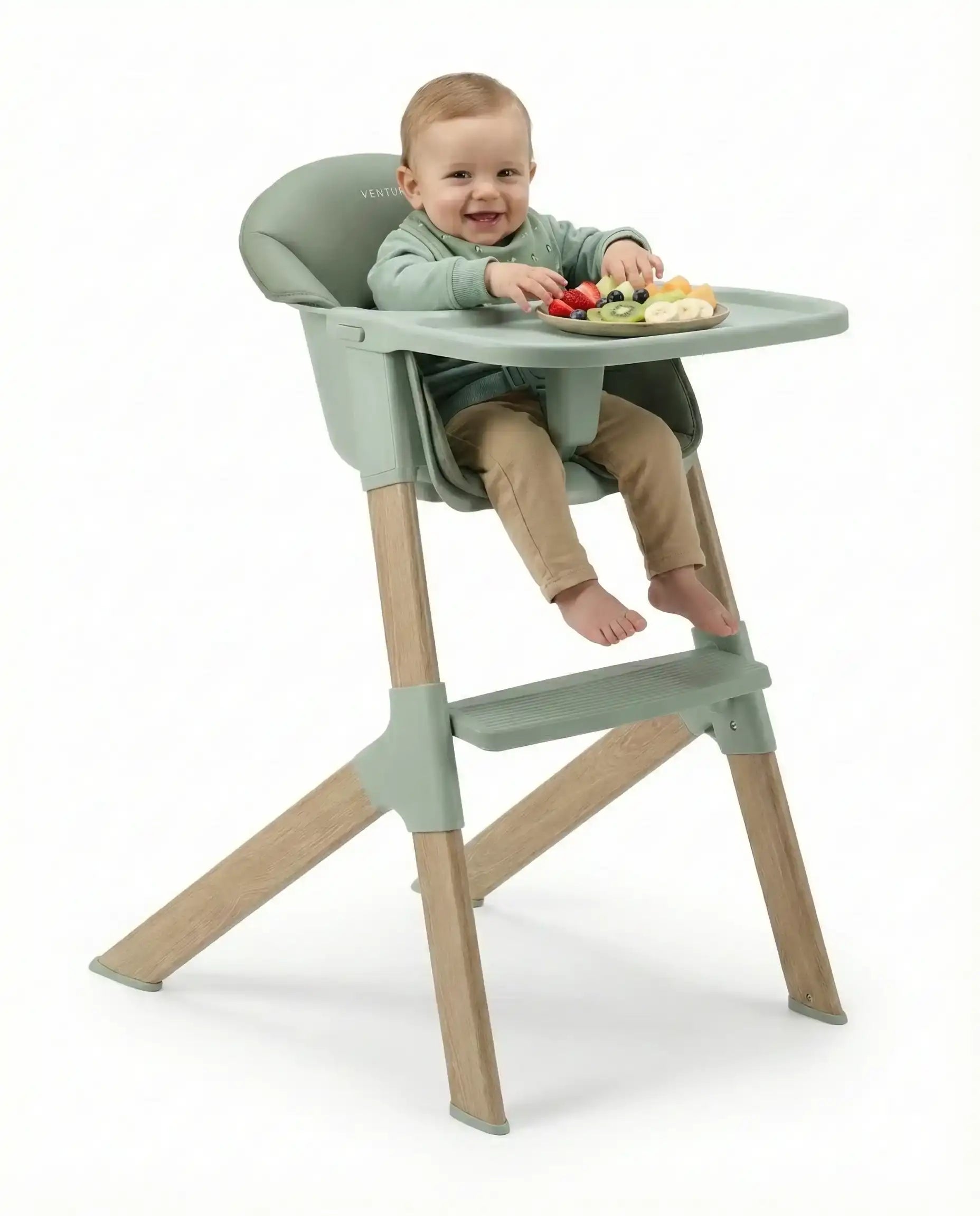Child in a green and beige high chair with a tray, sitting on a white background