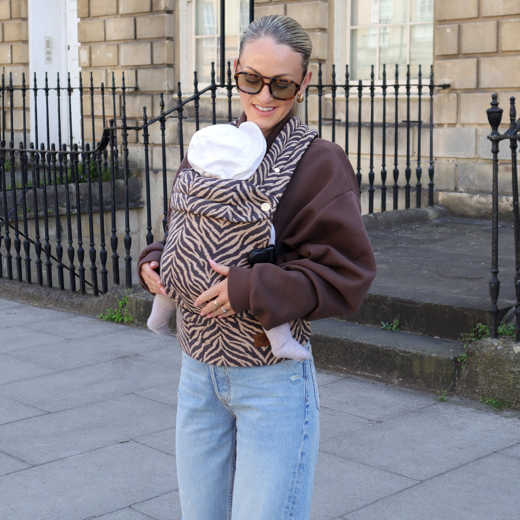Woman carrying a baby in a sling on a city street.